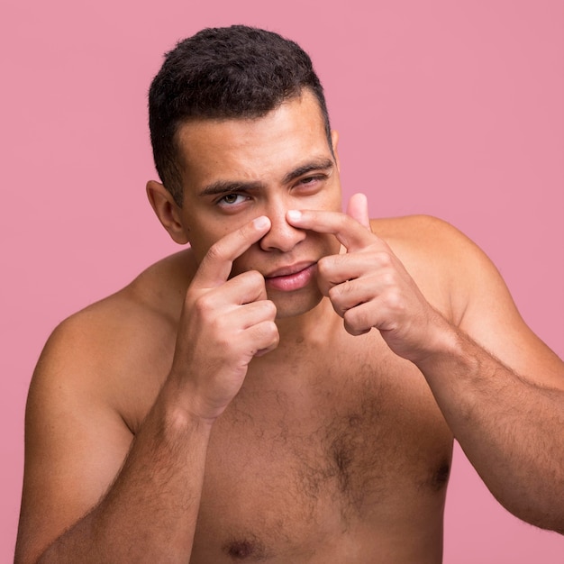 Vista frontal de um homem tentando estourar uma espinha no nariz