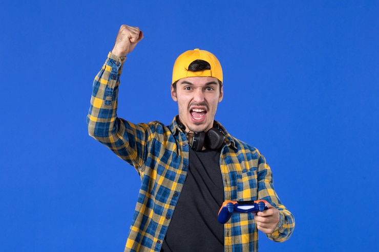 Foto grátis vista frontal de um jovem animado com gamepad jogando videogame na parede azul