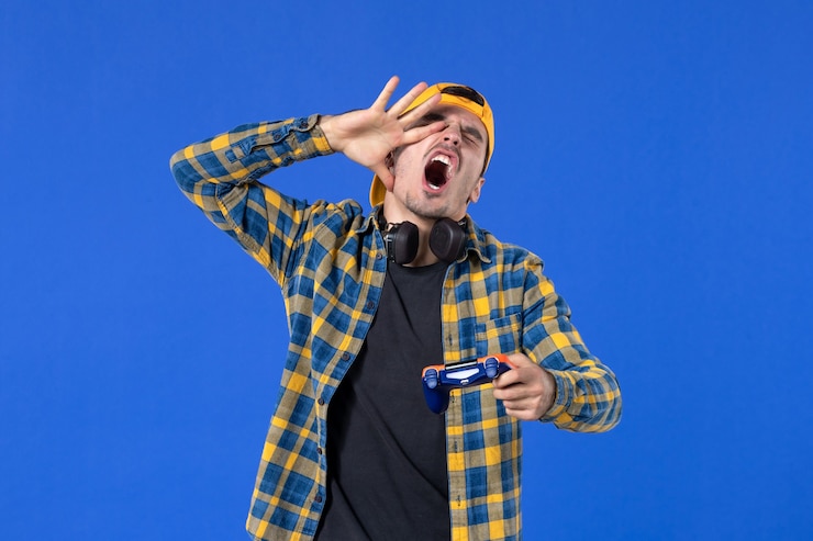 Foto grátis vista frontal de um jovem animado com gamepad jogando videogame na parede azul