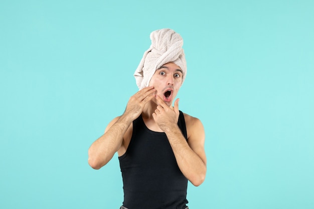 Vista frontal de um jovem após o banho com rosto surpreso na parede azul