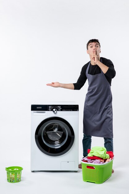 Vista frontal de um jovem com máquina de lavar e roupas sujas na parede branca