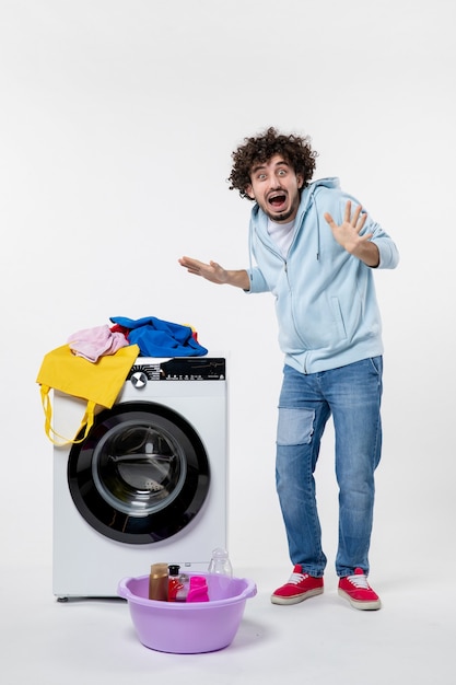 Vista frontal de um jovem com máquina de lavar e roupas sujas na parede branca