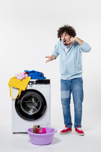 Foto grátis vista frontal de um jovem com máquina de lavar e roupas sujas na parede branca