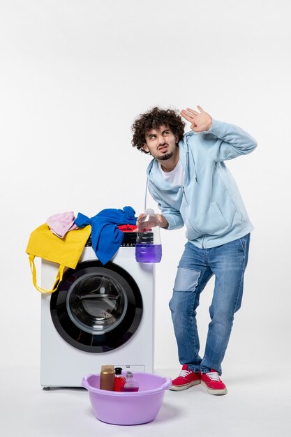 Vista frontal de um jovem com máquina de lavar segurando pó líquido na parede branca