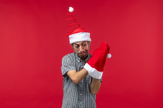 Vista frontal de um jovem com tampa vermelha de Natal na parede vermelha