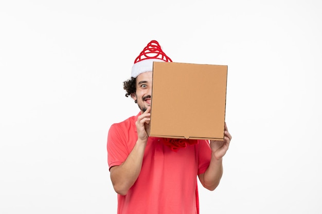 Vista frontal de um jovem com uma caixa de comida de entrega na parede branca