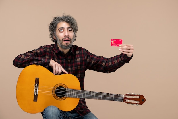 Vista frontal de um jovem com uma guitarra segurando um cartão vermelho do banco na parede rosa