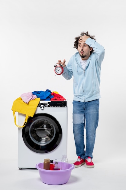 Vista frontal de um jovem com uma lavadora segurando relógios na parede branca