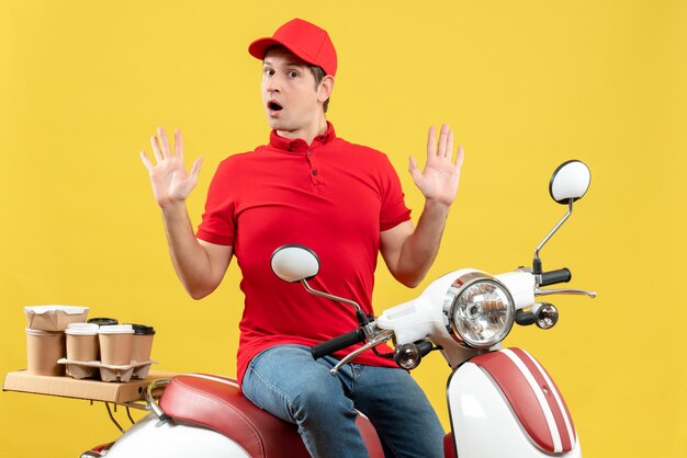 Vista frontal de um jovem curioso usando blusa vermelha e chapéu, entregando pedidos em fundo amarelo