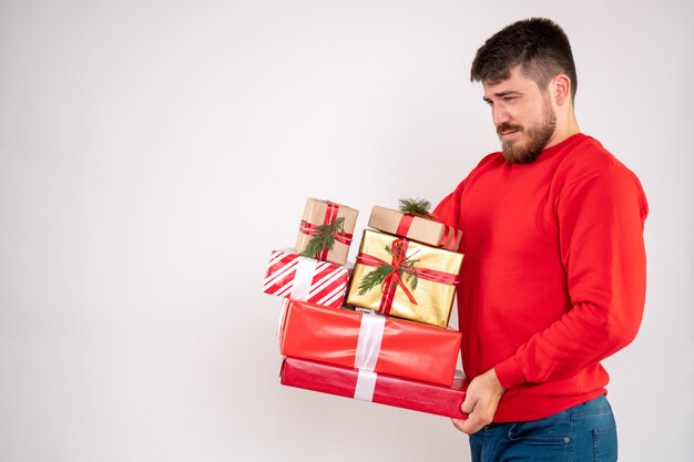 Vista frontal de um jovem de camisa vermelha segurando presentes de Natal na parede branca