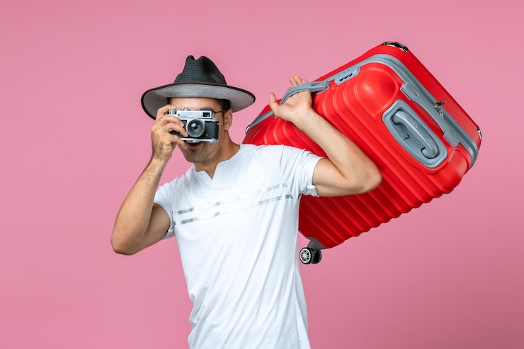 Foto grátis vista frontal de um jovem de férias tirando fotos segurando uma bolsa vermelha na parede rosa