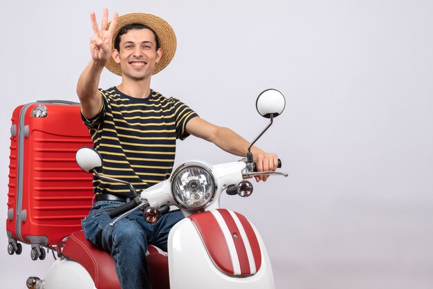 Vista frontal de um jovem feliz com chapéu de palha na motocicleta mostrando os dedos