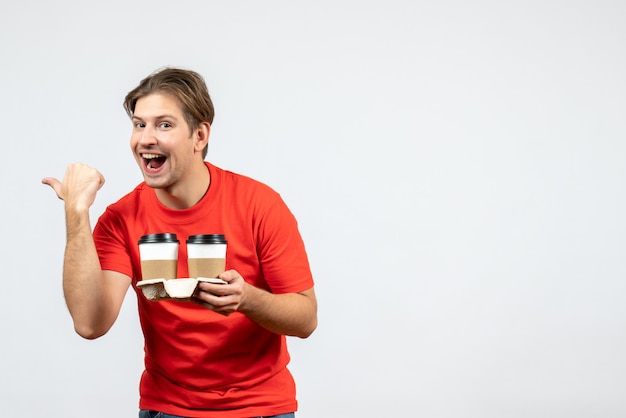 Vista frontal de um jovem feliz com uma blusa vermelha segurando uma pequena caixa e apontando para trás no fundo branco