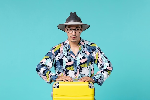 Vista frontal de um jovem homem com sua bolsa amarela se preparando para uma viagem em uma parede azul clara