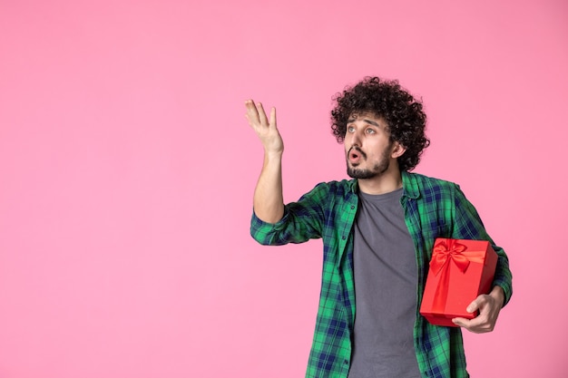 Vista frontal de um jovem homem com um pacote vermelho na parede rosa claro