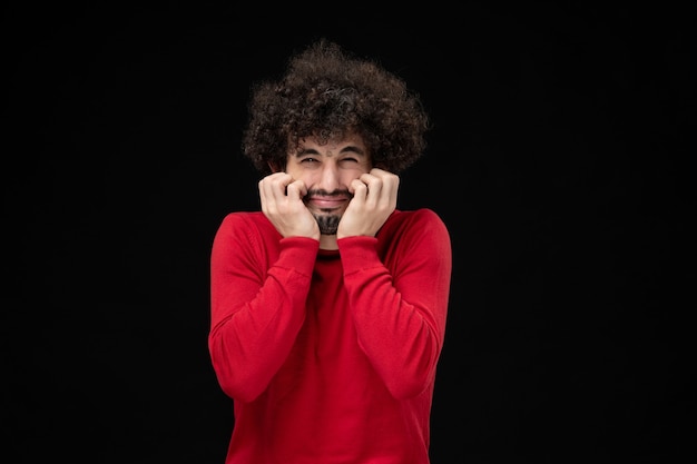 Vista frontal de um jovem homem com um suéter vermelho na parede preta