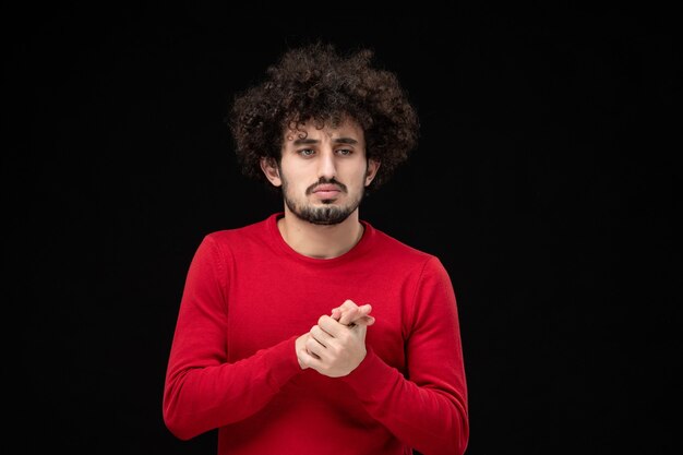 Vista frontal de um jovem homem com um suéter vermelho na parede preta