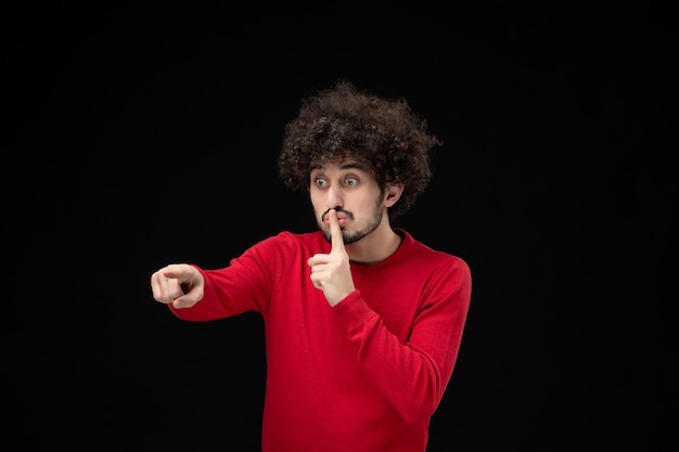 Vista frontal de um jovem homem com um suéter vermelho na parede preta