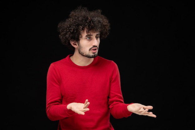 Vista frontal de um jovem homem com um suéter vermelho na parede preta