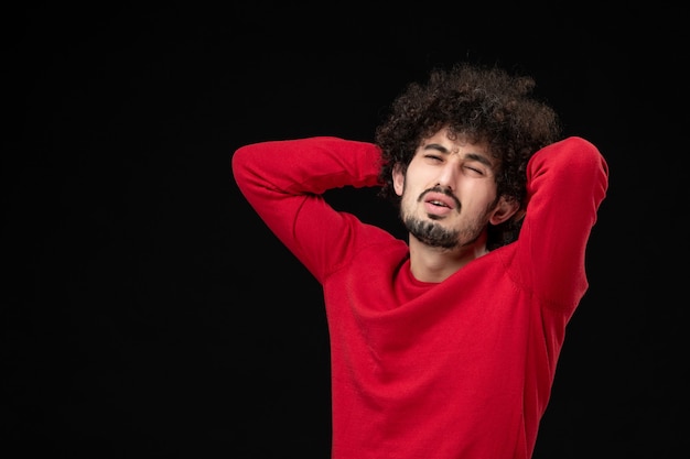 Vista frontal de um jovem homem com um suéter vermelho na parede preta