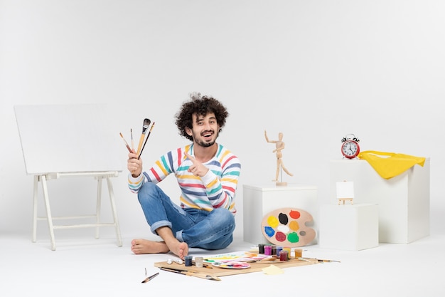 Vista frontal de um jovem homem desenhando pinturas na parede branca