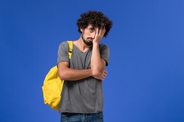 Foto grátis vista frontal de um jovem homem em uma camiseta cinza usando uma mochila amarela deprimida na parede azul