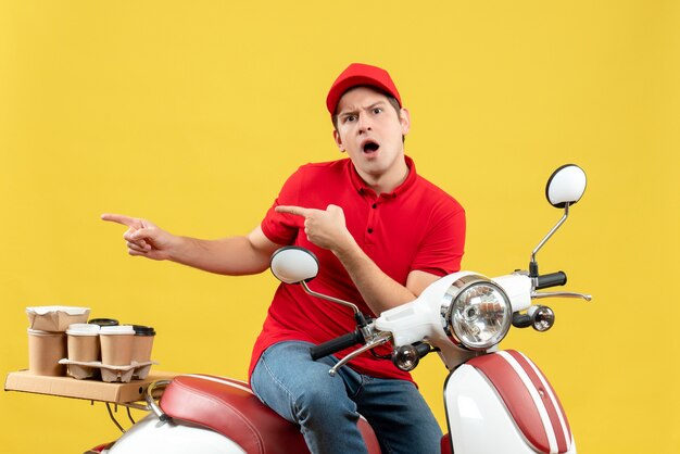 Vista frontal de um jovem imaginando um rapaz com blusa vermelha e chapéu entregando pedidos, apontando algo no lado direito sobre fundo amarelo