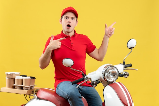 Vista frontal de um jovem imaginando um rapaz de blusa vermelha e chapéu, entregando pedidos, apontando para cima em um fundo amarelo