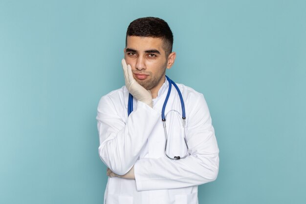 Vista frontal de um jovem médico de terno branco com estetoscópio azul e expressão deprimida