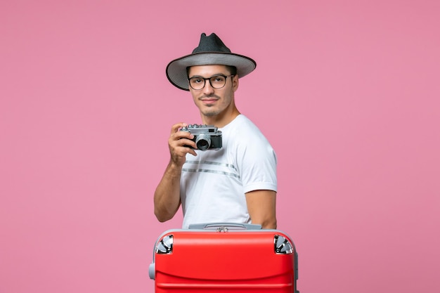 Vista frontal de um jovem nas férias de verão tirando fotos com a câmera na parede rosa