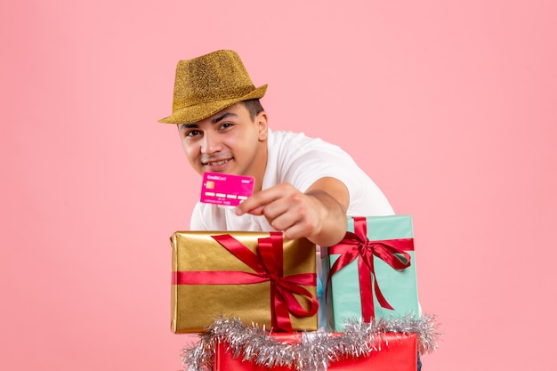 Vista frontal de um jovem perto do Natal apresenta segurando um cartão do banco na parede rosa