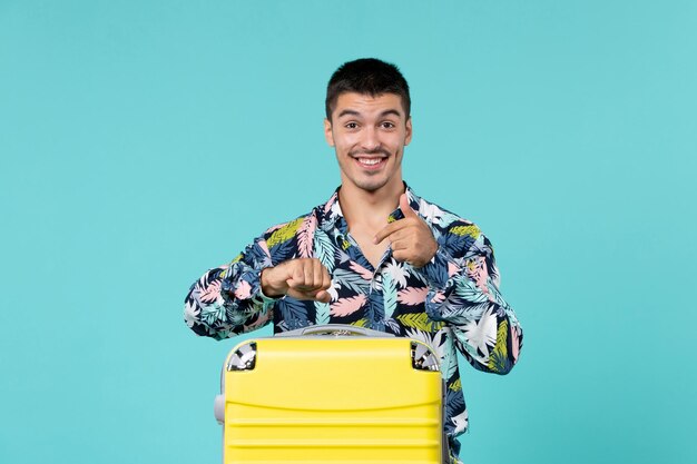 Vista frontal de um jovem se preparando para as férias com sua bolsa amarela na parede azul