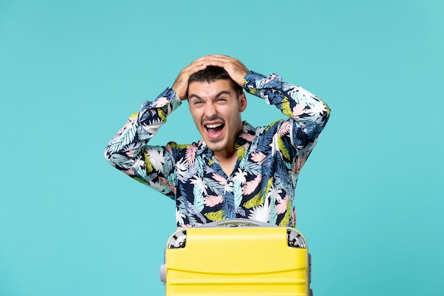 Vista frontal de um jovem se preparando para as férias com uma bolsa gritando na parede azul