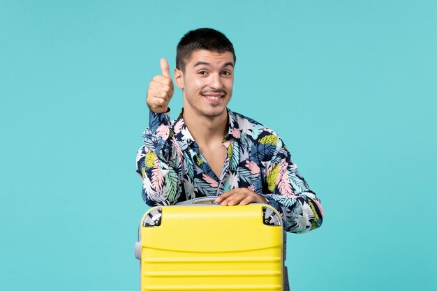 Vista frontal de um jovem se preparando para uma viagem com sua bolsa amarela na parede azul clara