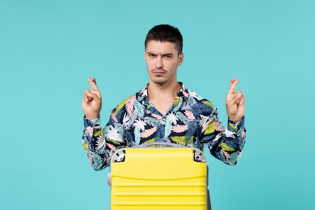 Vista frontal de um jovem se preparando para uma viagem com sua bolsa amarela na parede azul clara