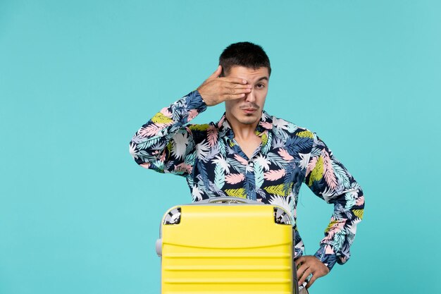 Vista frontal de um jovem se preparando para uma viagem com sua bolsa amarela na parede azul