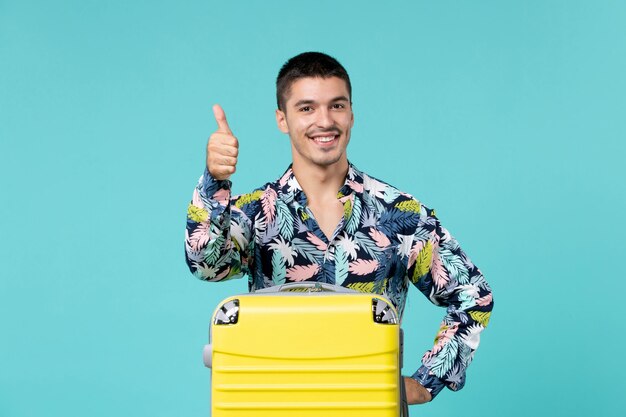 Vista frontal de um jovem se preparando para uma viagem com sua bolsa amarela sorrindo na parede azul