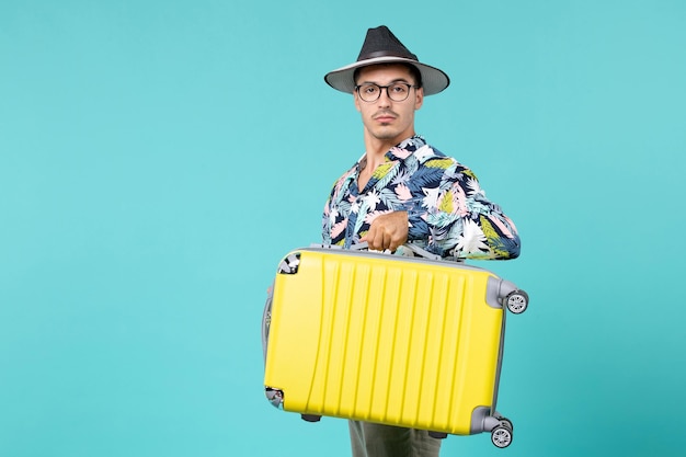 Vista frontal de um jovem se preparando para uma viagem e segurando sua bolsa na parede azul