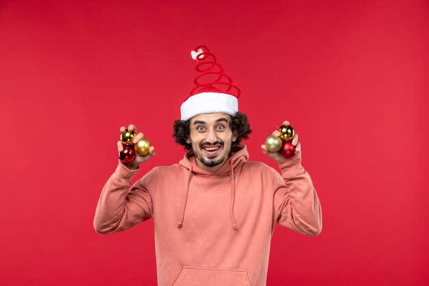 Vista frontal de um jovem segurando brinquedos da árvore de Natal na parede vermelha