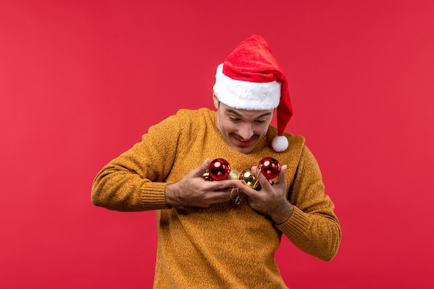 Vista frontal de um jovem segurando brinquedos da árvore de Natal na parede vermelha