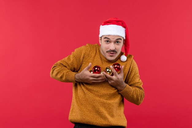 Vista frontal de um jovem segurando brinquedos da árvore de Natal na parede vermelha