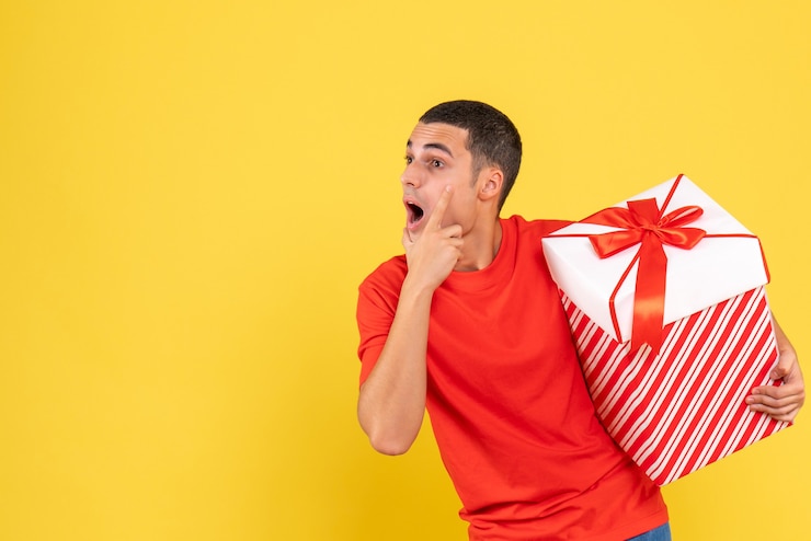 Foto grátis vista frontal de um jovem segurando um grande presente de natal na parede amarela