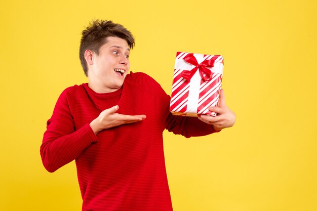 Vista frontal de um jovem segurando um presente de Natal na parede amarela