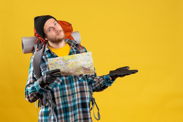 Vista frontal de um jovem turista feliz com luvas de couro e uma mochila segurando o mapa
