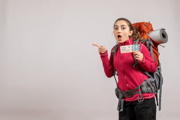 Vista frontal de um jovem viajante perplexo com uma grande mochila segurando uma passagem