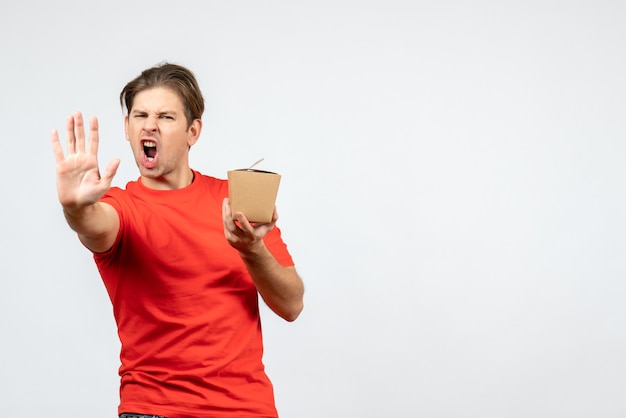 Vista frontal de um jovem zangado com uma blusa vermelha, segurando uma pequena caixa e mostrando cinco em fundo branco