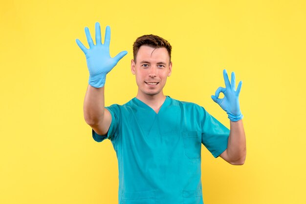Vista frontal de um médico com luvas azuis na parede amarela