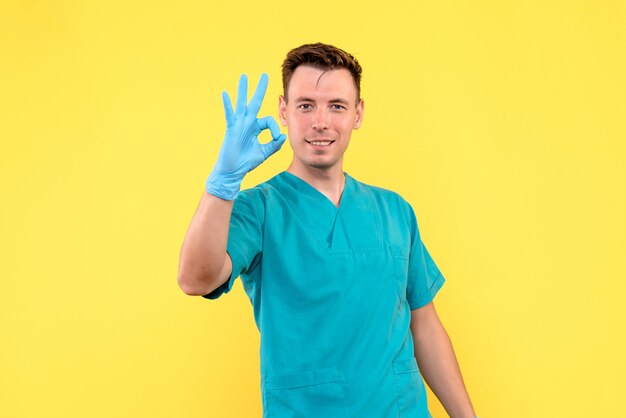 Vista frontal de um médico com luvas azuis na parede amarela