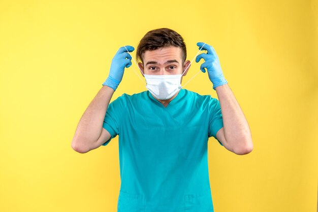 Vista frontal de um médico com luvas e máscara na parede amarela