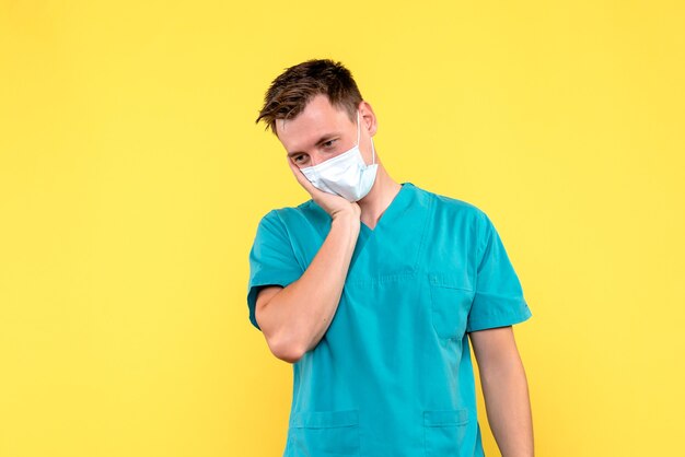 Vista frontal de um médico com máscara estéril na parede amarela